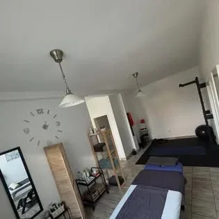 Miestnosť ambulancie s masážnym stolom, policami a nástennými hodinami